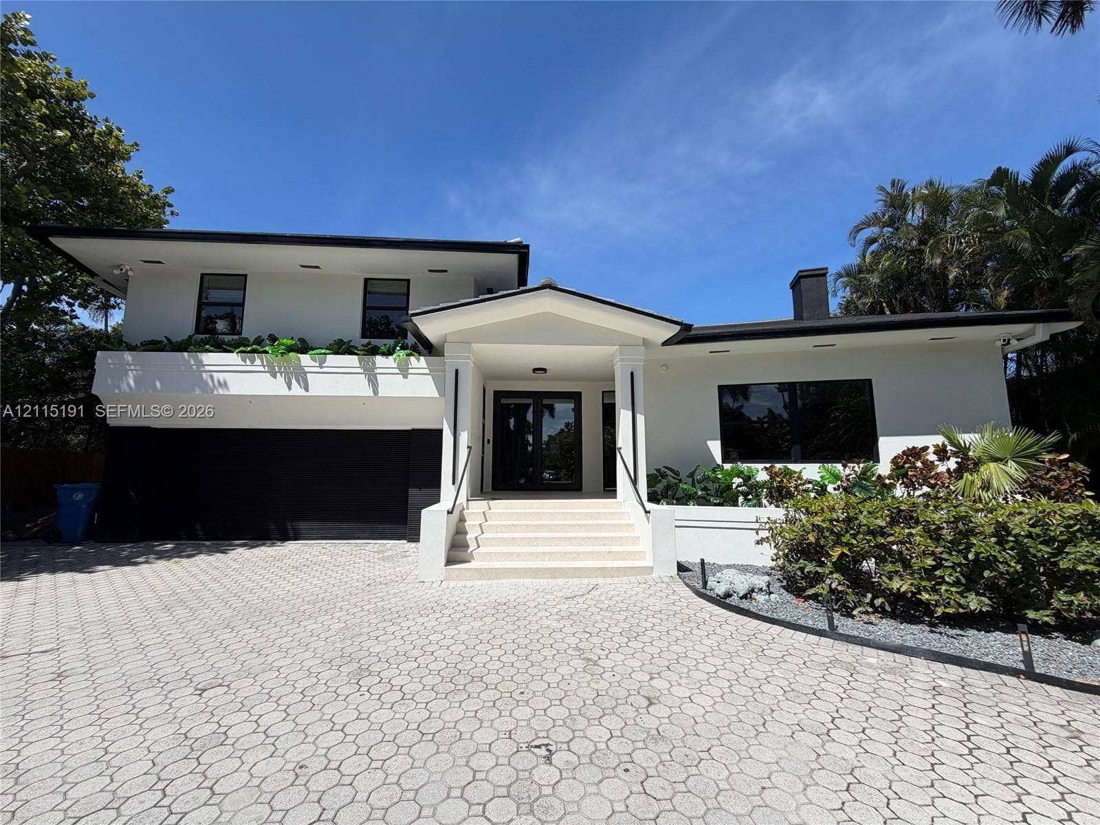 451 Center Island Drive, Golden Beach, FL 33160 Two-story exterior featuring white stucco finish, geometric paver driveway, recessed lighting, integrated garage, and a covered entryway with concrete steps
