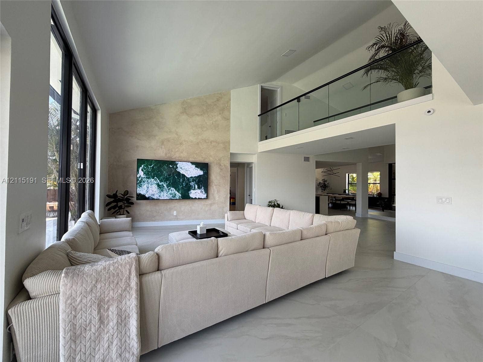 451 Center Island Drive, Golden Beach, FL 33160 Double-height ceiling, textured accent wall, floor-to-ceiling windows, porcelain tile flooring, and glass-paneled interior railing