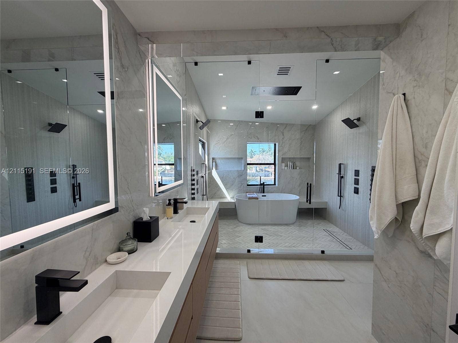 451 Center Island Drive, Golden Beach, FL 33160 Dual-vanity cabinet with white composite countertops, integrated rectangular sinks, and matte black fixtures, paired with backlit vanity mirrors