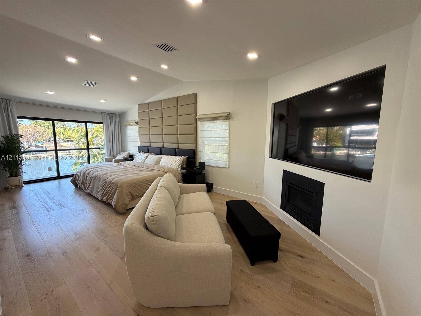 451 Center Island Drive, Golden Beach, FL 33160 Vaulted ceilings with recessed lighting, wood-finish flooring, custom upholstered wall paneling, built-in fireplace, and expansive black-framed sliding glass doors