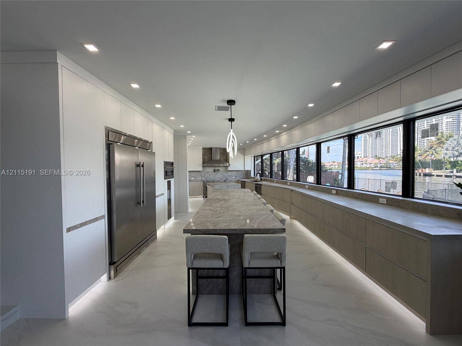451 Center Island Drive, Golden Beach, FL 33160 Kitchen featuring matte-finish cabinetry, a large stone-topped central island, integrated stainless steel appliances, recessed lighting, and expansive windows
