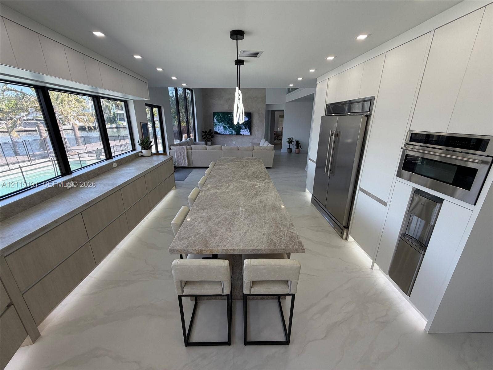 451 Center Island Drive, Golden Beach, FL 33160 Contemporary kitchen featuring floor-to-ceiling cabinetry, a central stone-topped island with integrated base lighting, stainless steel appliances, and large-format tile flooring