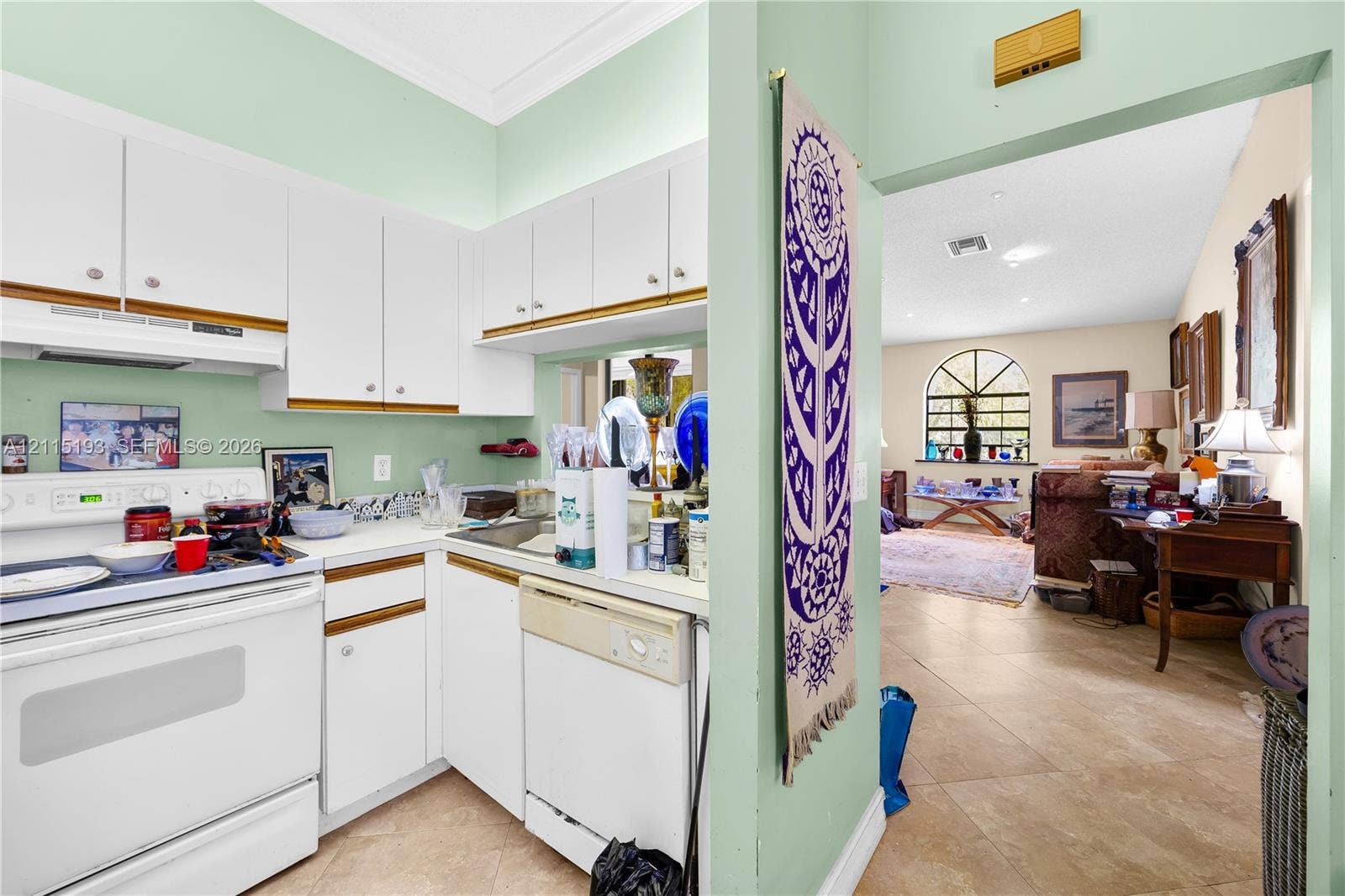 5422 Venetia Court, #G, Boynton Beach, FL 33437 Kitchen featuring white cabinetry, integrated white appliances, and a pass-through opening, with tile flooring visible in the common area