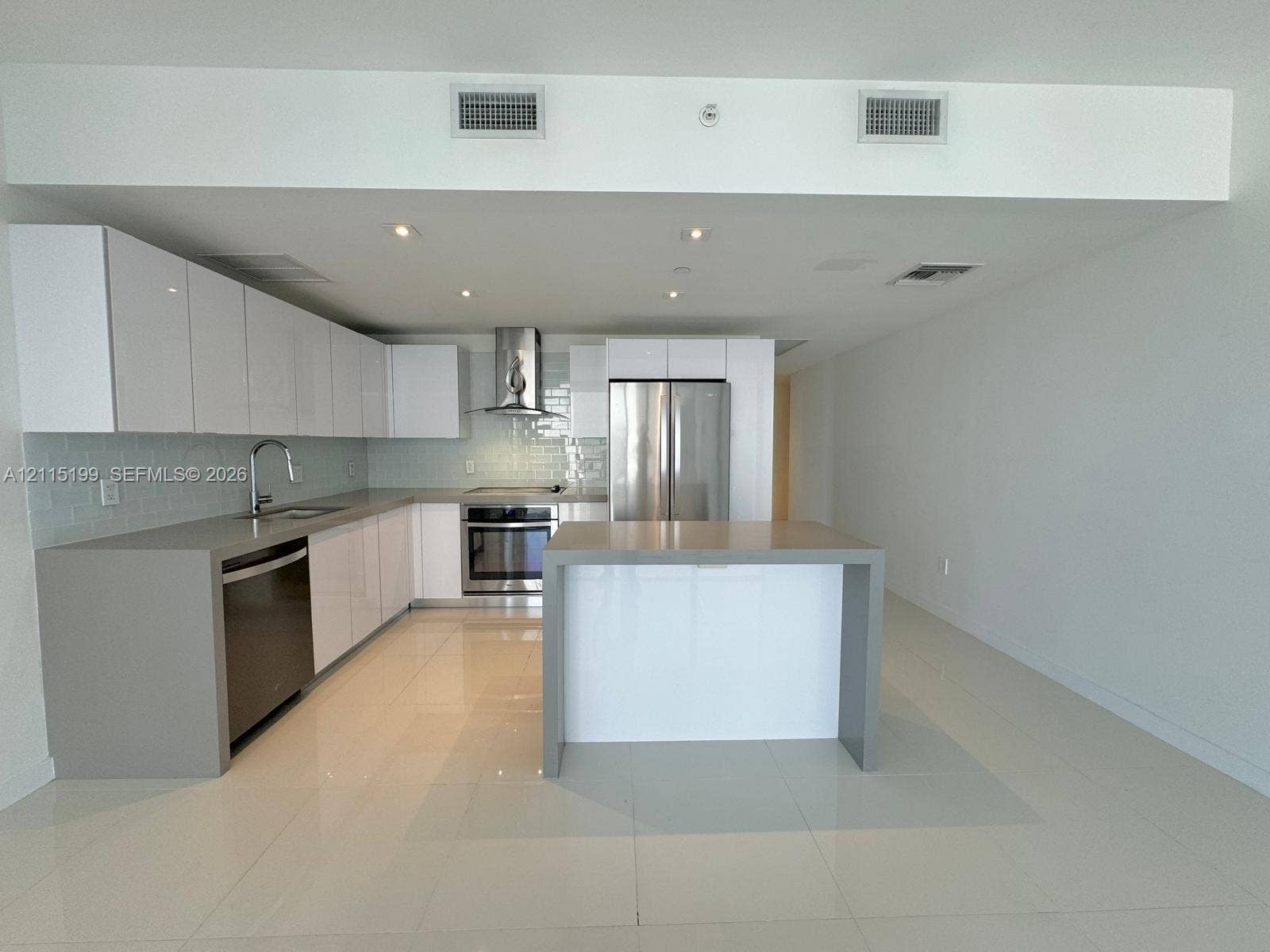 1600 NE 1st Avenue, #3120, Miami, FL 33132 Contemporary kitchen featuring high-gloss white cabinetry, expansive stone-finish countertops, stainless steel appliances, a subway tile backsplash, and a large central island