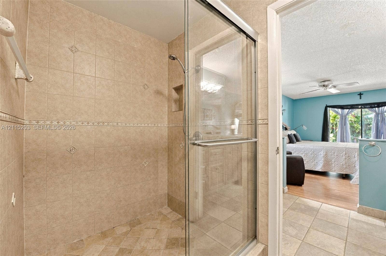 Walk-in shower featuring glass enclosure, ceramic tile surround with decorative accent inlay, recessed shelving, and a handheld shower fixture