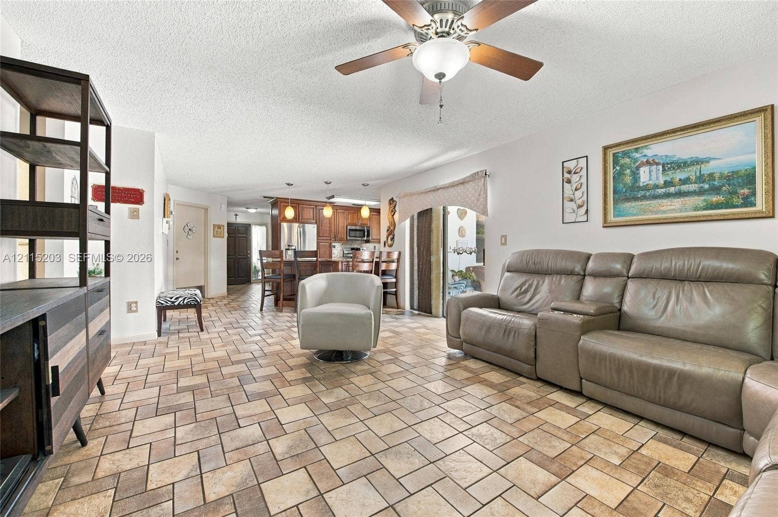 Open-concept interior featuring stone-tile flooring in a herringbone pattern, wood-finish cabinetry, built-in recessed lighting, and a ceiling fan with integrated lighting