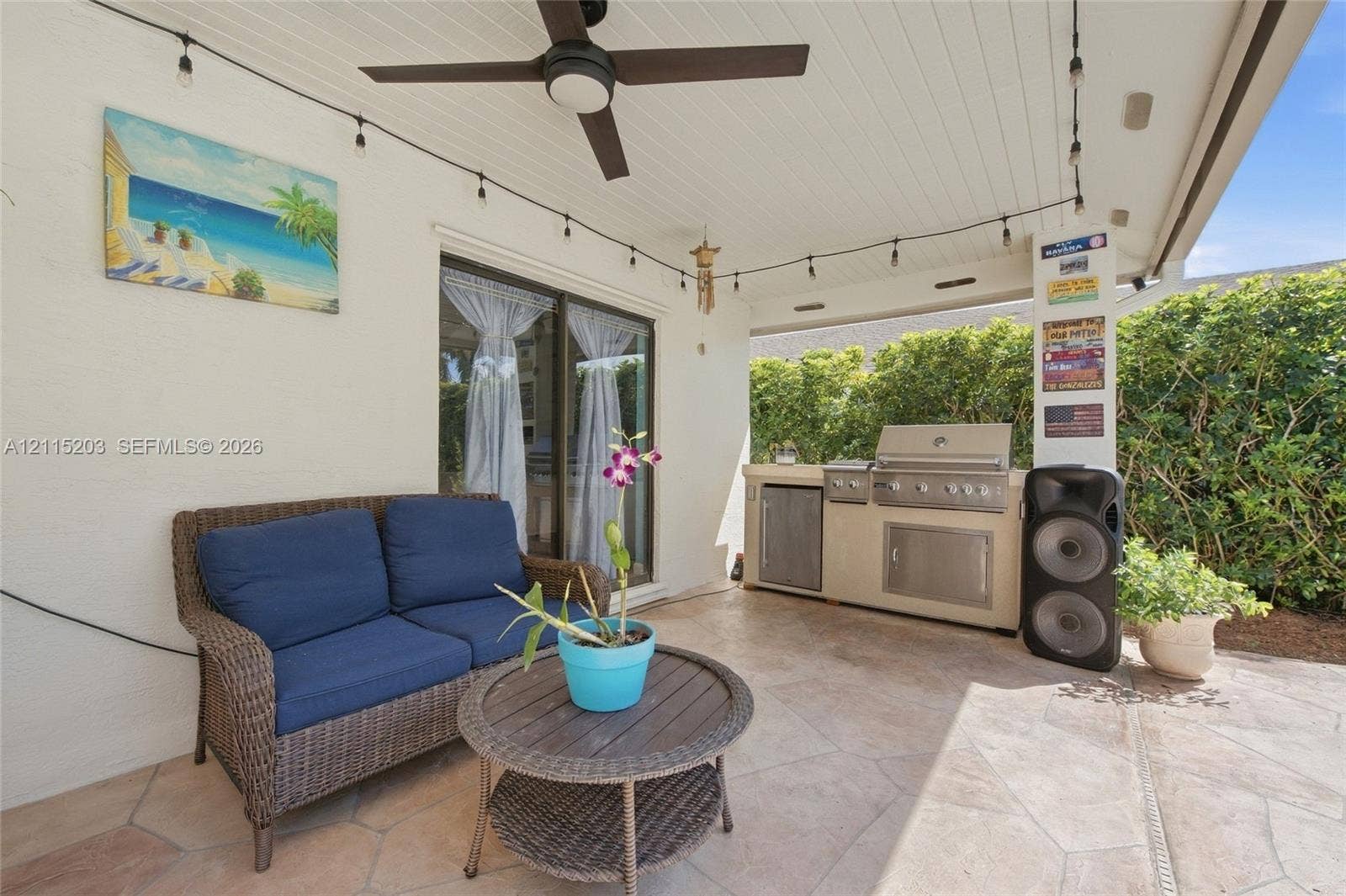 Covered outdoor patio featuring flagstone-style flooring, built-in stainless steel grill station with under-counter storage, ceiling fan, and beadboard ceiling