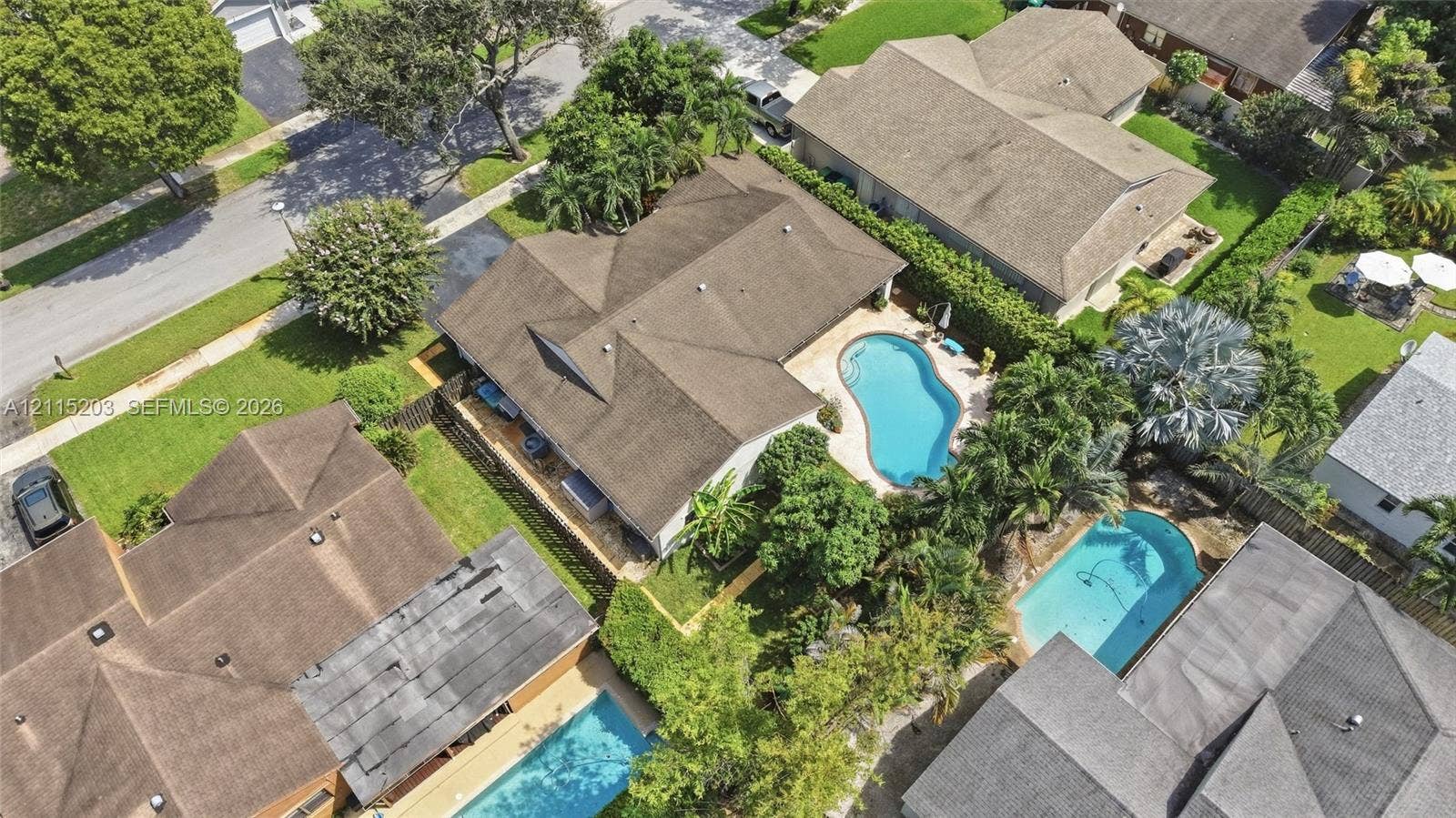 Aerial perspective featuring a multi-hipped roofline, an in-ground swimming pool, a concrete patio area, and mature perimeter landscaping