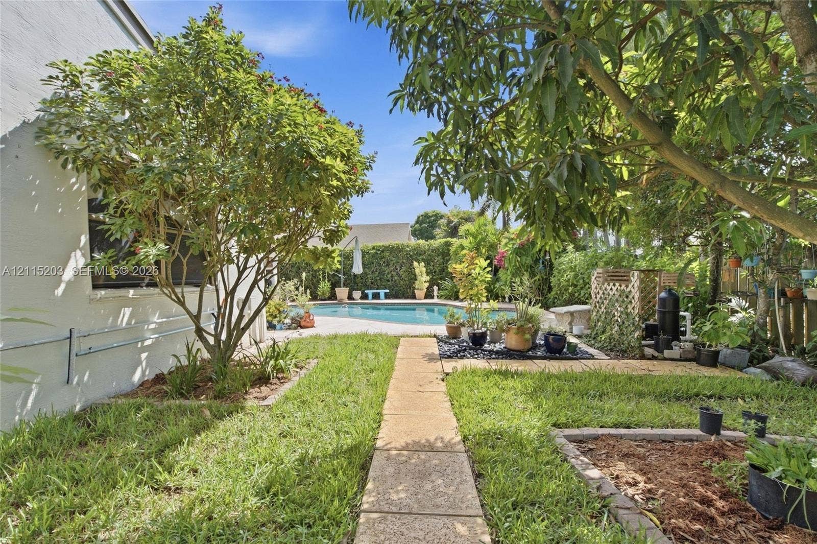 Backyard featuring an in-ground swimming pool, concrete paver walkway, landscaped garden beds, and mature fruit trees