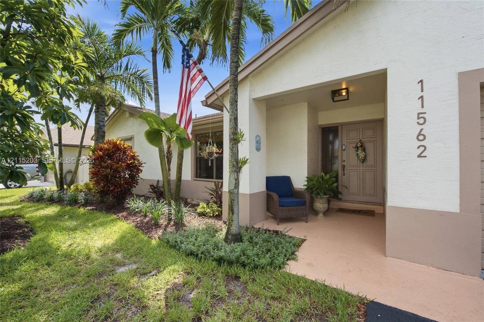 Recessed covered entryway, multi-paneled front door, and mature tropical landscaping with lighting
