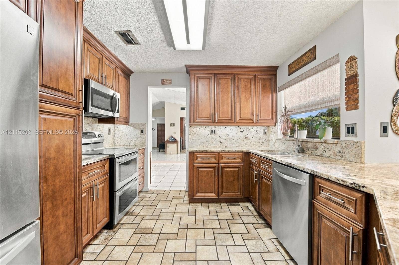 Kitchen featuring warm-tone wood cabinetry, natural stone countertops, stainless steel appliances, and tiled flooring