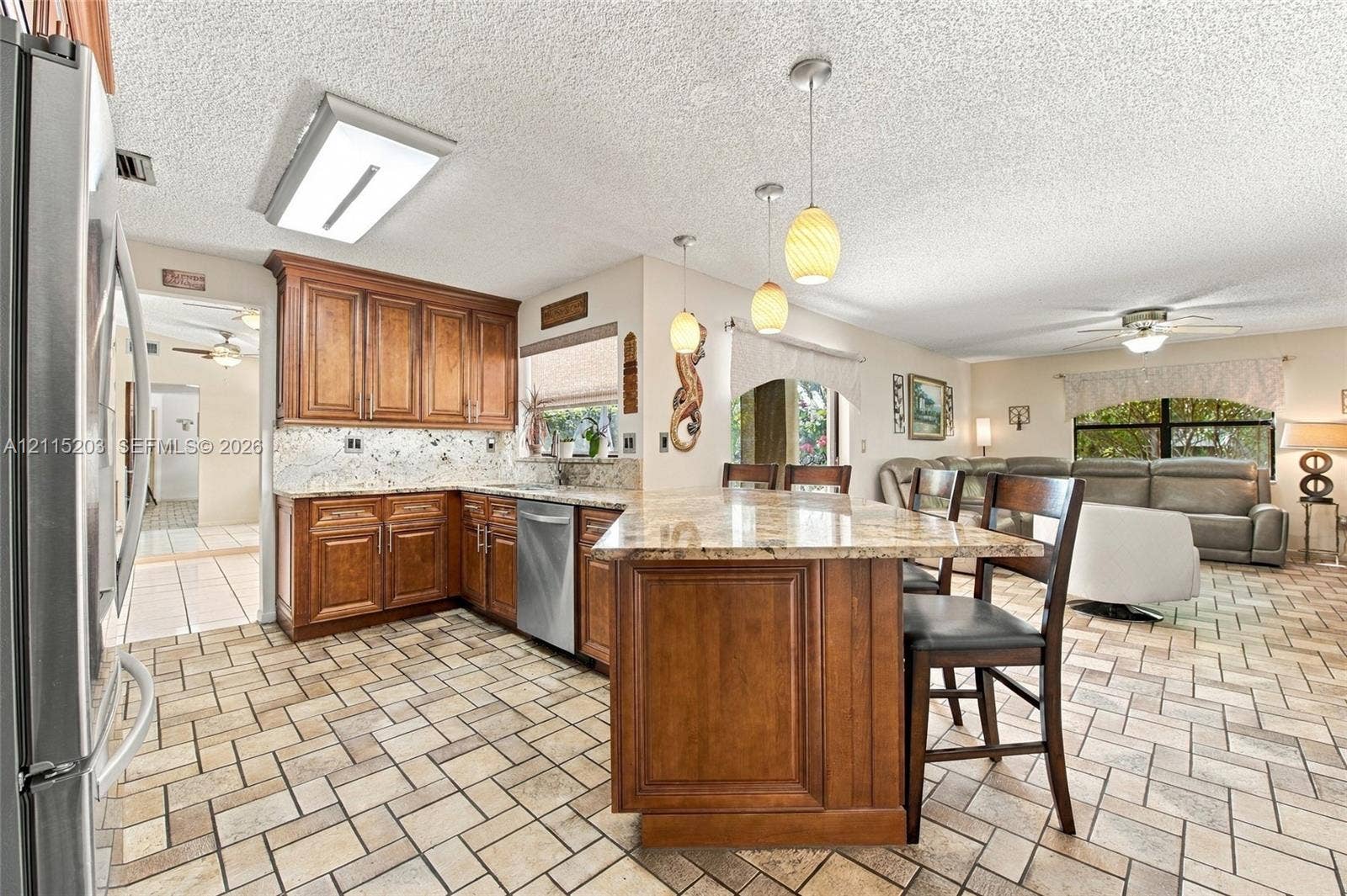 Kitchen featuring natural stone countertops, custom wood cabinetry, stainless steel dishwasher, stone-tile flooring, and glass pendant lighting