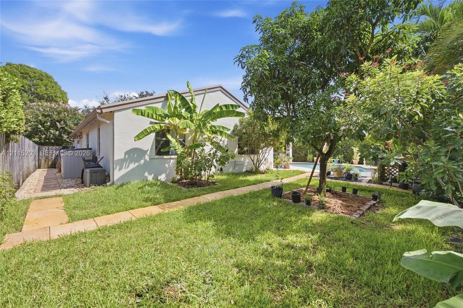 Backyard featuring a paved stone walkway, established landscaping, mature fruit trees, wood fence, and a swimming pool