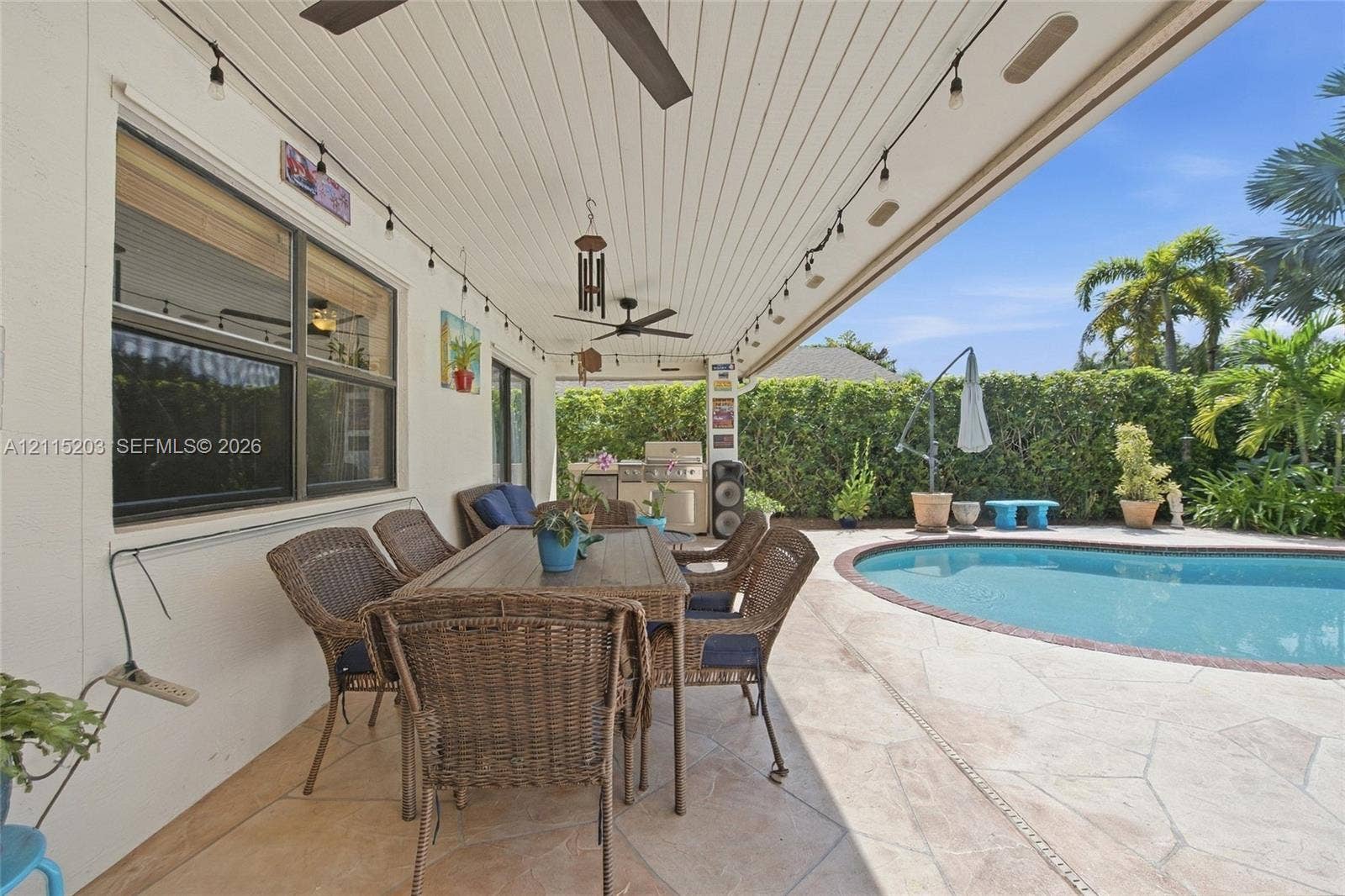 Covered patio featuring a tongue-and-groove ceiling, stone-tiled flooring, built-in outdoor kitchen, string lighting, and an inground pool with a stone deck