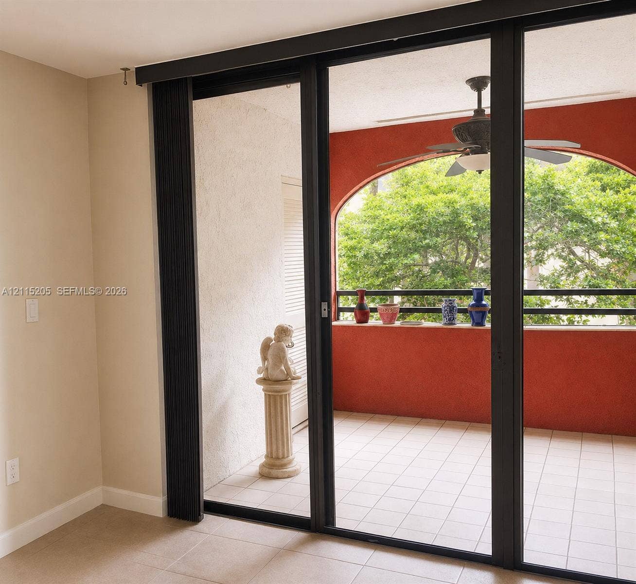 Sliding glass doors open to a covered and screened in balcony with a tiled floor, arched architectural detailing, and an integrated ceiling fan