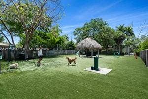 6330 SW 79th Street, #20, South Miami, South Miami, FL 33143 Fenced outdoor recreation area featuring synthetic turf, a thatched-roof pavilion, mature trees, and a water station