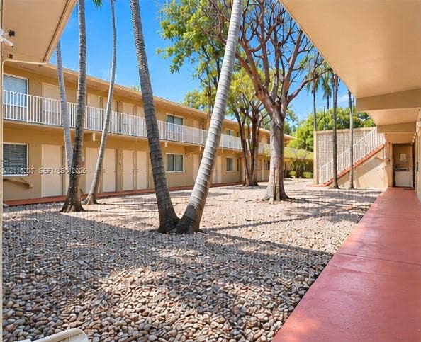 6330 SW 79th Street, #20, South Miami, South Miami, FL 33143 Open-air courtyard featuring gravel ground cover, mature palm trees, tiered exterior walkways with white metal railings, and a concrete staircase