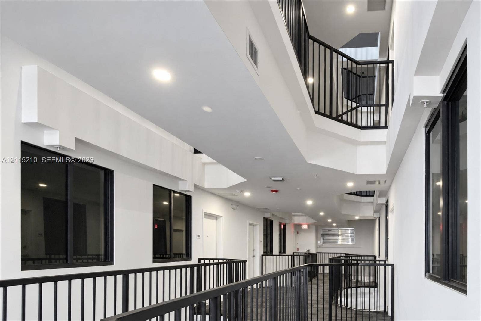 136 NW 26th Street, #507, Miami, FL 33127 Multi-level walkway featuring black metal railings, recessed ceiling lighting, and large windows with black frames