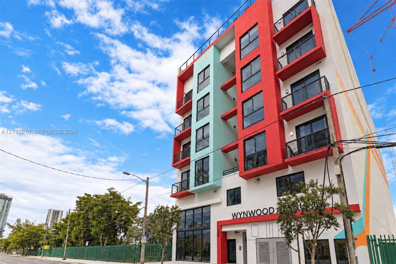 136 NW 26th Street, #507, Miami, FL 33127 Multi-story contemporary exterior featuring a bold red and teal facade, private balconies with glass railings, floor-to-ceiling ground-level windows, and a flat roofline