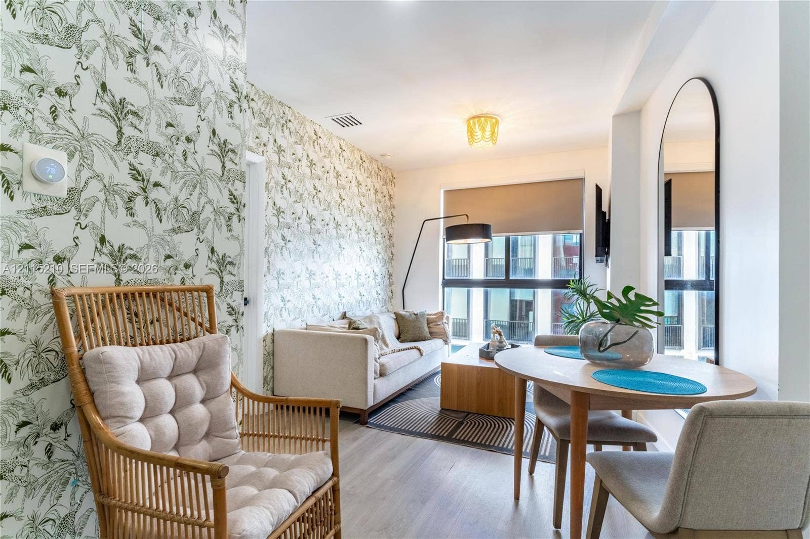 136 NW 26th Street, #507, Miami, FL 33127 Patterned botanical wallpaper, wood-finish flooring, floor-to-ceiling windows with roller shades, a flush-mount geometric ceiling light fixture, and an arched wall-mounted mirror
