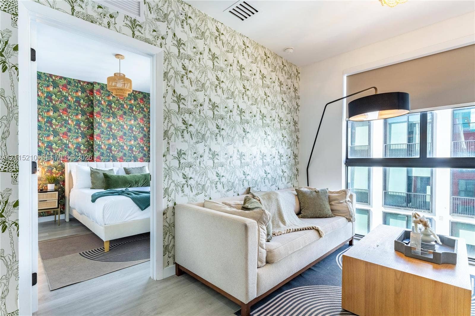 136 NW 26th Street, #507, Miami, FL 33127 Interior space featuring large-format windows with roller shades, botanical patterned wallpaper, and light-toned wood-finish flooring