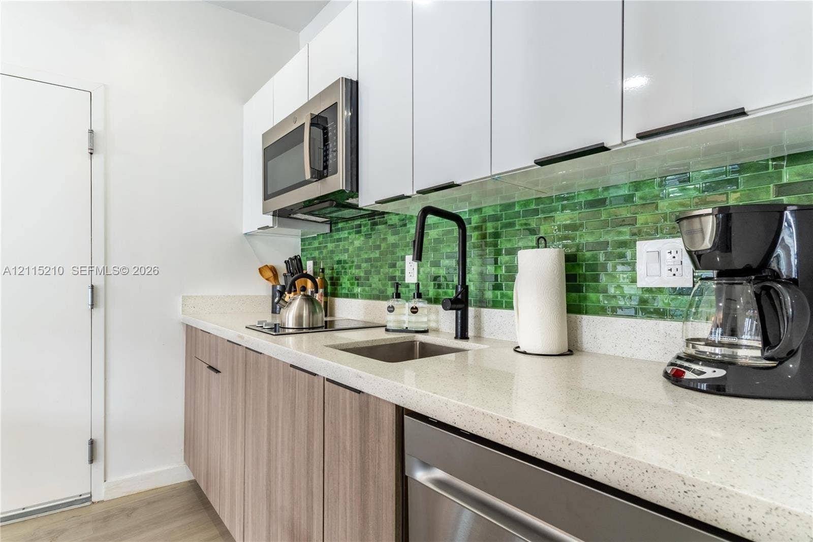 136 NW 26th Street, #507, Miami, FL 33127 Kitchen featuring white high-gloss upper cabinetry, wood-finish lower cabinetry, stone-composite countertops, a glass subway-tile backsplash, and a matte black gooseneck faucet