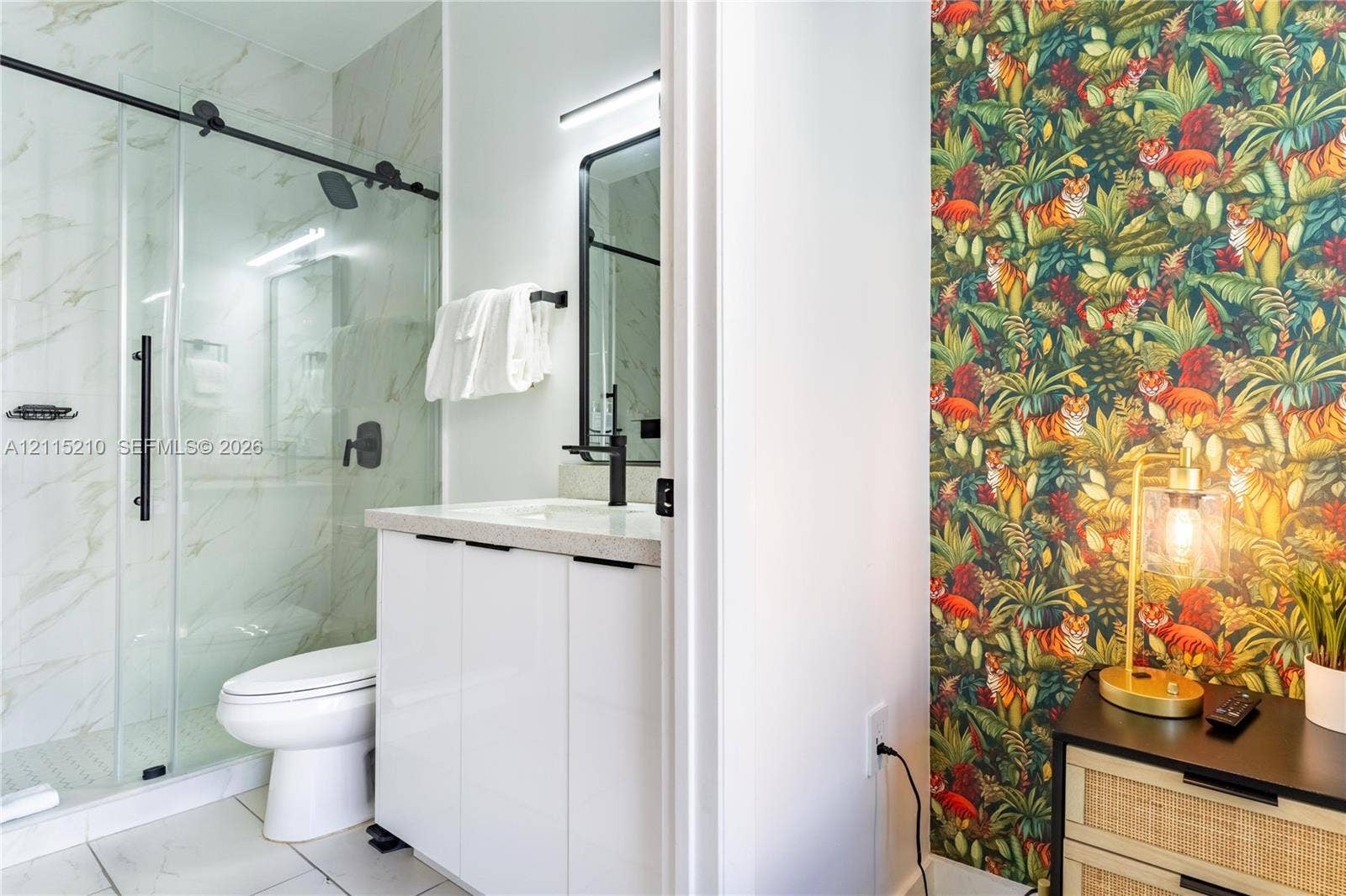 136 NW 26th Street, #507, Miami, FL 33127 Bathroom featuring a glass-enclosed shower with sliding hardware, stone-finish countertop, white cabinetry, matte black fixtures, and large-format tile flooring