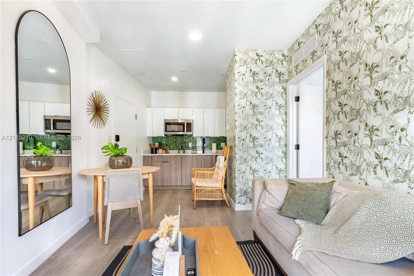 136 NW 26th Street, #507, Miami, FL 33127 Kitchen featuring white upper cabinetry, wood-finish lower cabinetry, green tile backsplash, and a built-in microwave, complemented by wood-finish flooring and patterned wall coverings