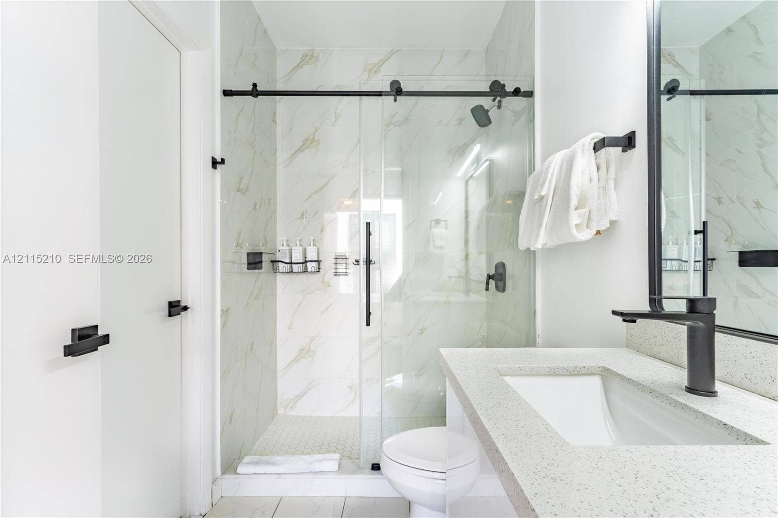 136 NW 26th Street, #507, Miami, FL 33127 Bathroom featuring a stone-composite countertop, undermount sink, matte black faucet, glass-enclosed shower with sliding barn-style door, and large-format wall tile