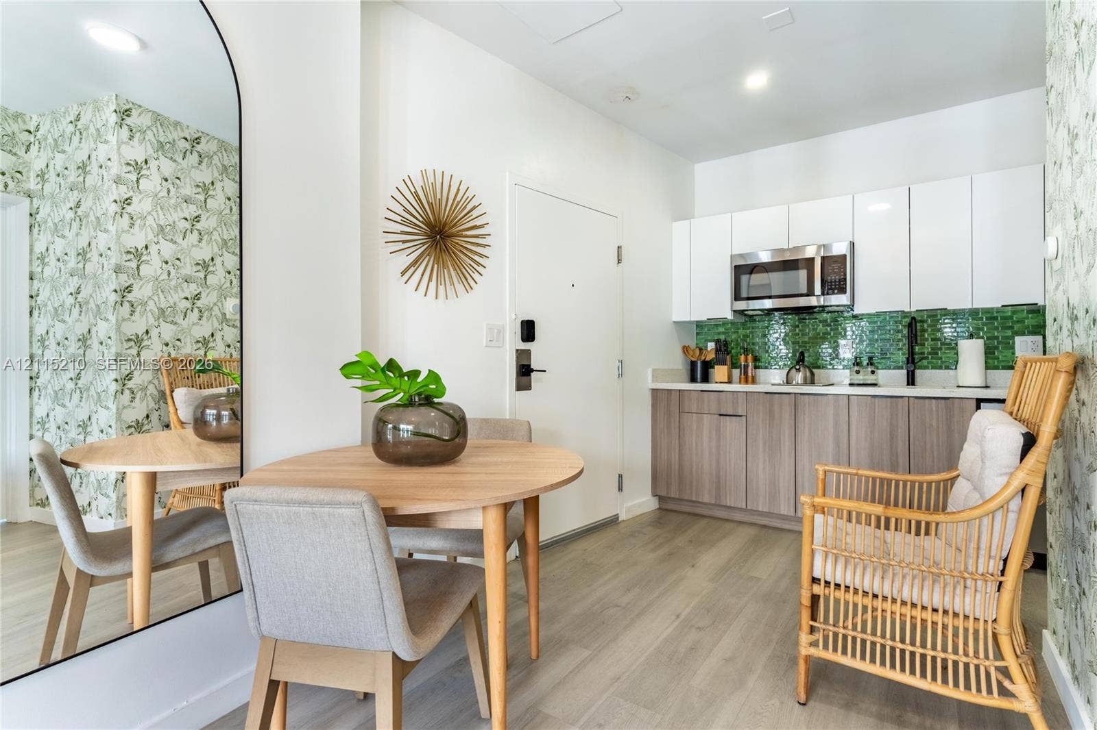 136 NW 26th Street, #507, Miami, FL 33127 Kitchen area featuring two-tone cabinetry, stainless steel microwave, green glass tile backsplash, wood-finish flooring, and arched floor mirror
