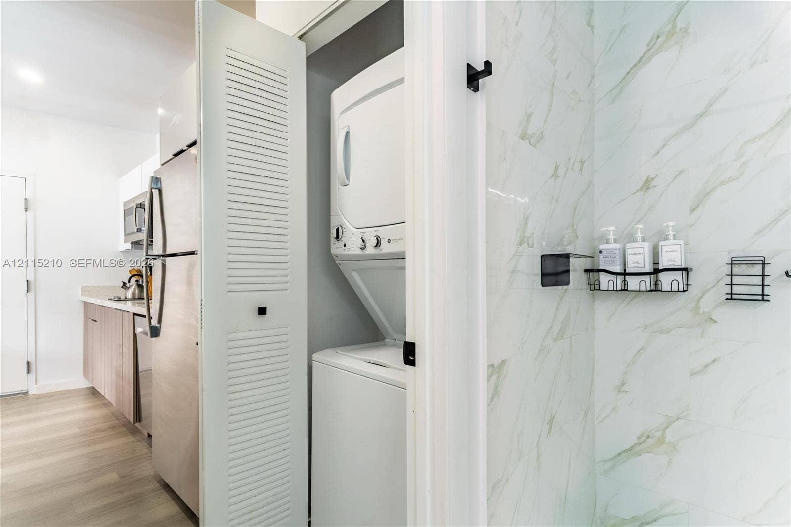 136 NW 26th Street, #507, Miami, FL 33127 Stacked laundry unit concealed behind louvered doors, stone-finish wall tile, and built-in matte black wall-mounted shelving