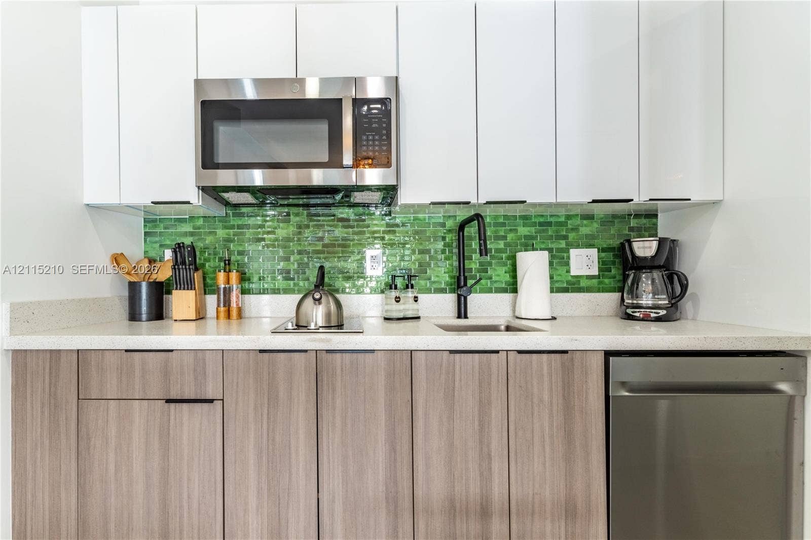 136 NW 26th Street, #507, Miami, FL 33127 Kitchen featuring white flat-panel cabinetry, wood-finish lower cabinetry, a green glass tile backsplash, light-toned stone-finish countertops, and stainless steel appliances