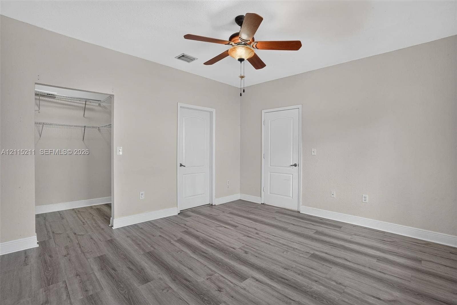 Neutral-toned interior featuring wood-finish flooring, a multi-blade ceiling fan with integrated lighting, two-panel interior doors, and a built-in closet with wire shelving