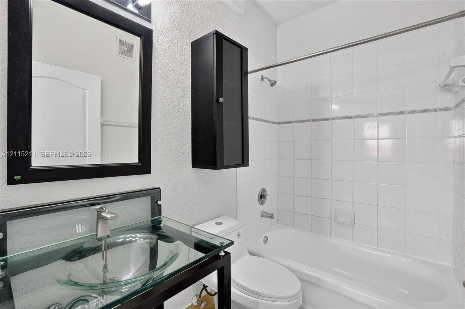 Bathroom featuring a glass vessel sink, dark-finish metal vanity frame, wall-mounted cabinet, and white tile shower surround