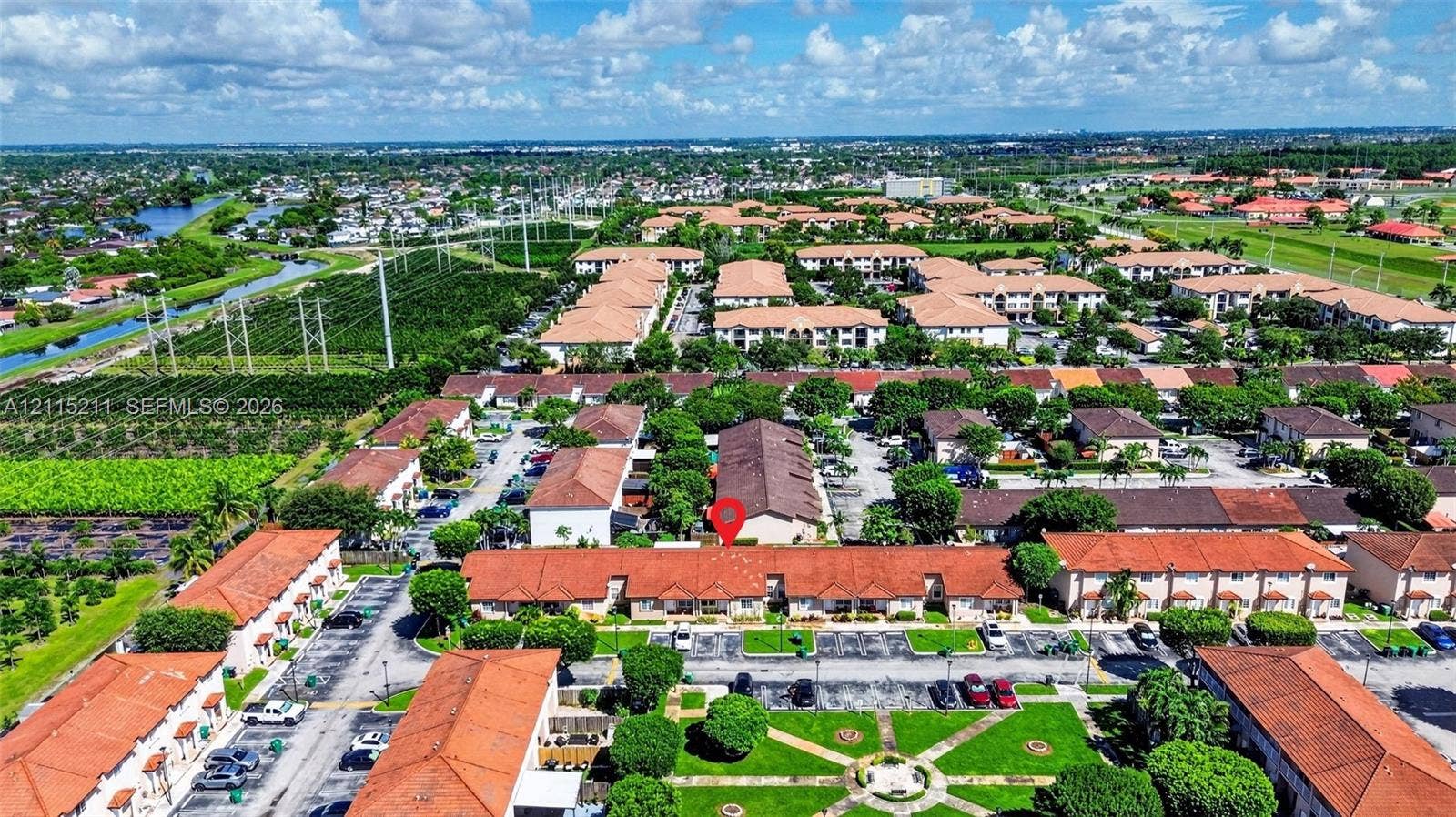 Aerial perspective featuring a multi-unit complex with red-tiled rooflines, paved parking areas, and manicured green spaces