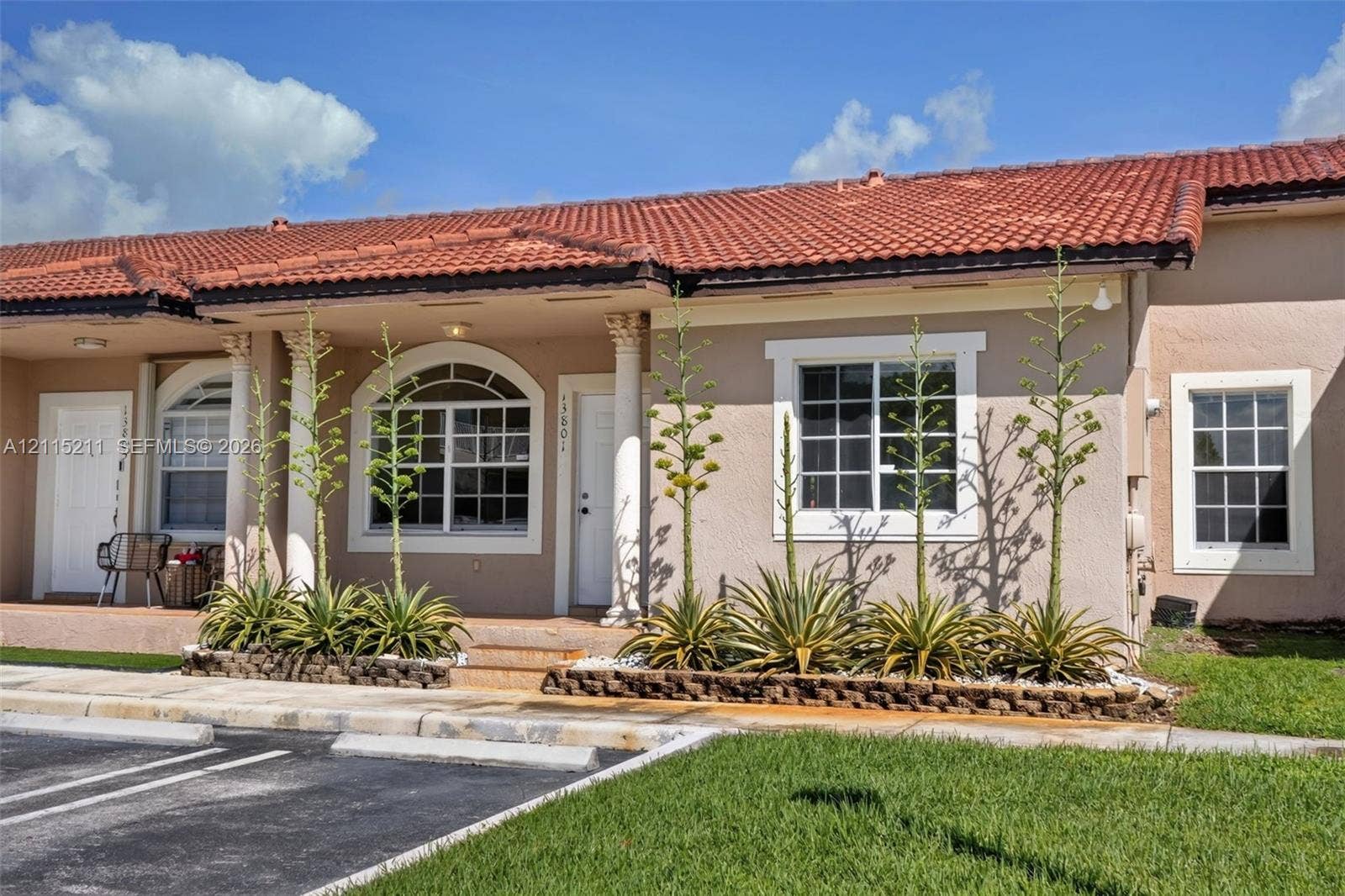 Stucco exterior featuring a red tile roof, decorative columns, arched window detailing, and raised stone garden beds