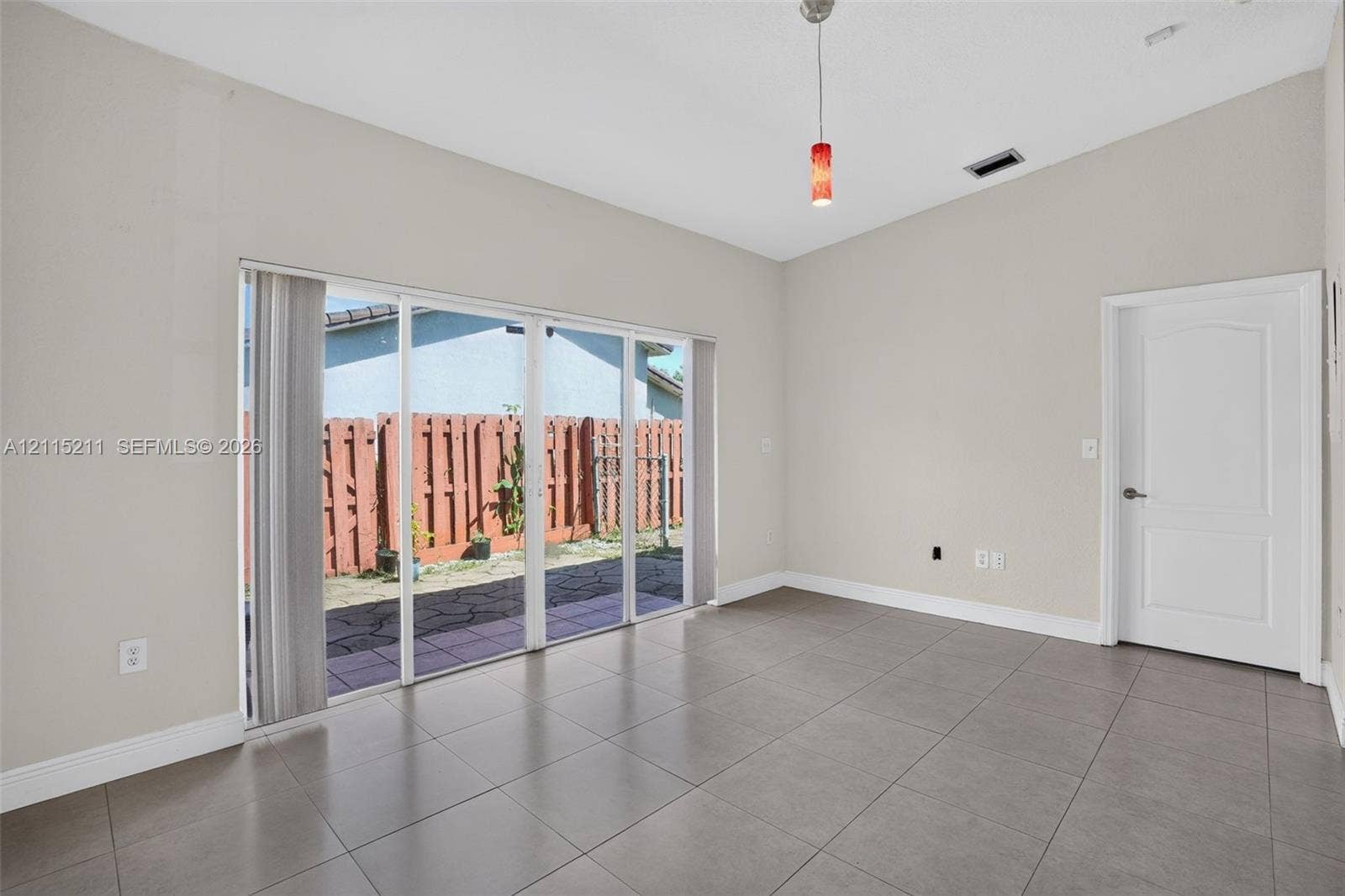 Vaulted ceilings, large-format tile flooring, sliding glass door with external access, and a single-pendant light fixture
