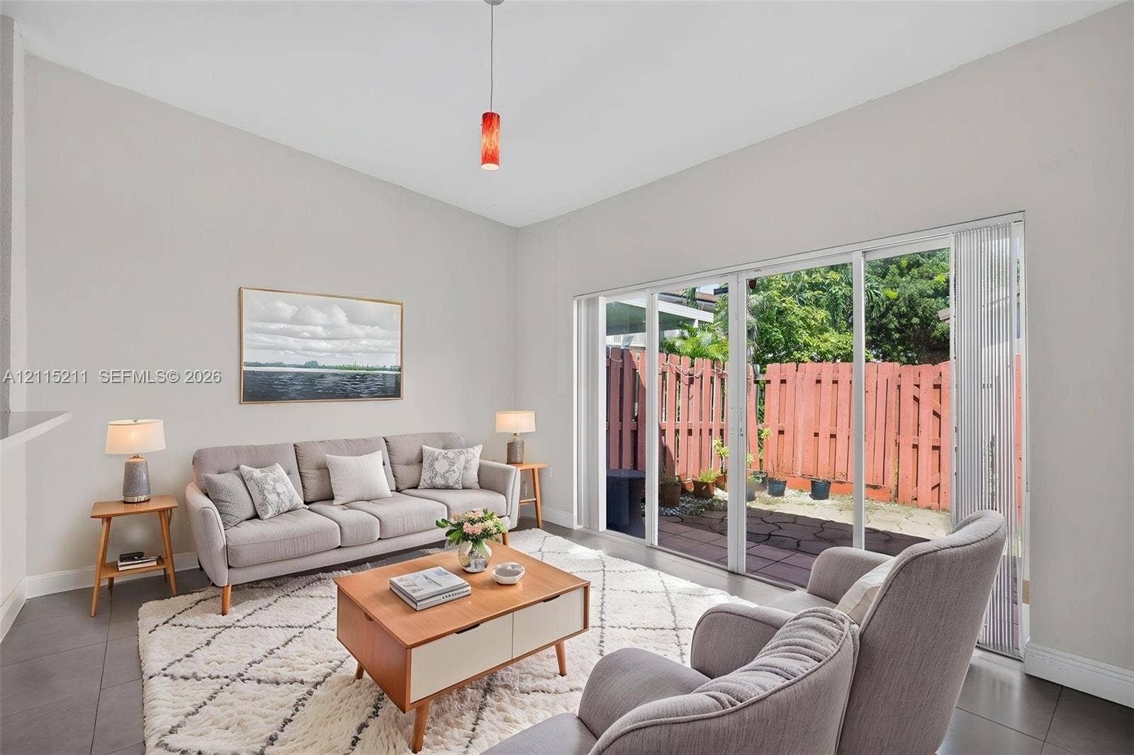 Living space featuring vaulted ceilings, large-format tile flooring, a glass pendant light, and a set of sliding glass doors opening to a fenced-in patio
