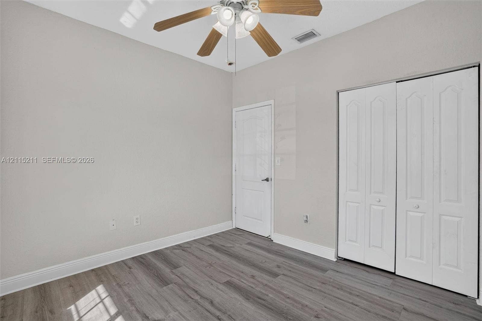Neutral-toned room featuring wood-finish flooring, a vaulted ceiling, a ceiling fan with integrated lighting, and a bi-fold closet