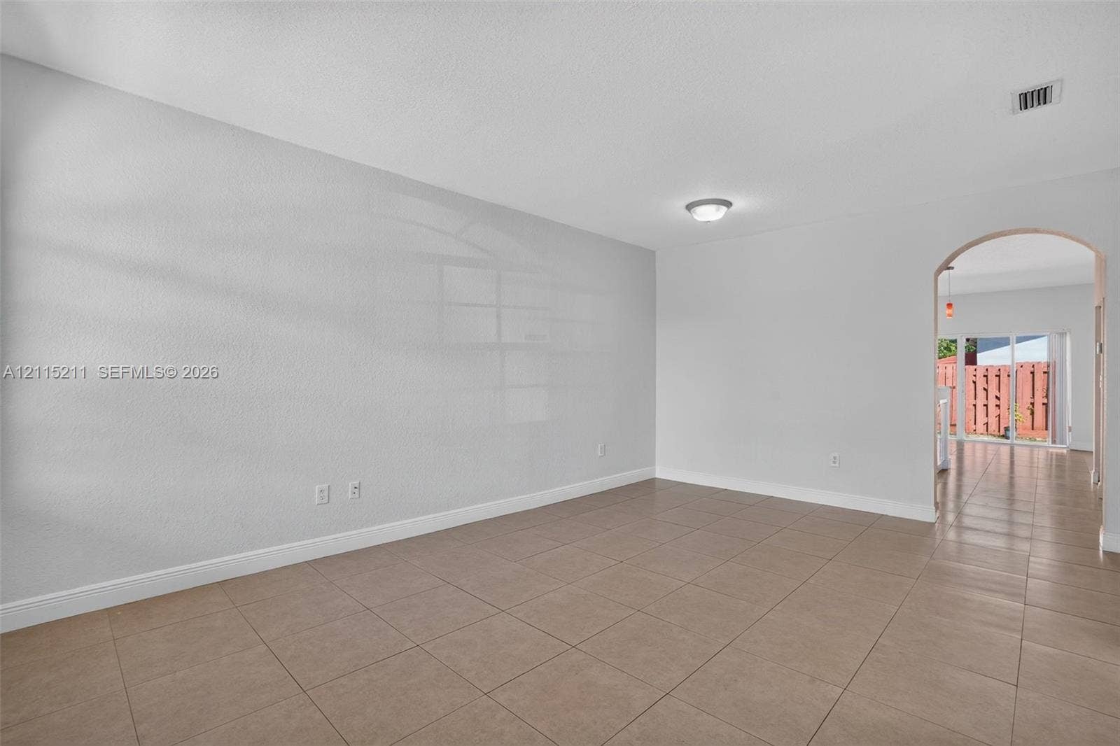 Neutral-toned interior space featuring large-format ceramic floor tiles, a structural arched doorway, and a ceiling-mounted light fixture