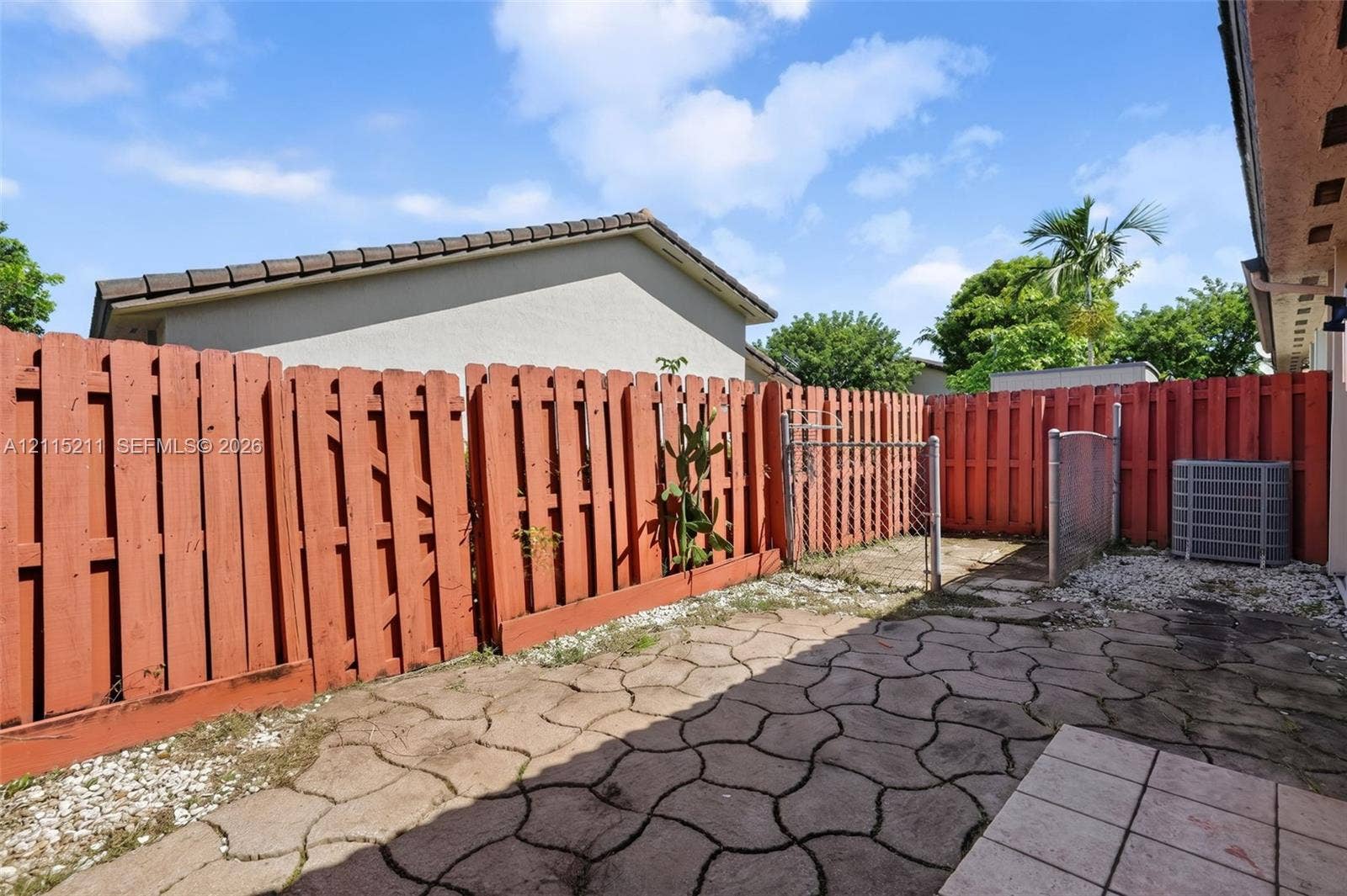 Private outdoor space featuring stained wood privacy fencing, decorative paver hardscaping, and a metal chain-link gate