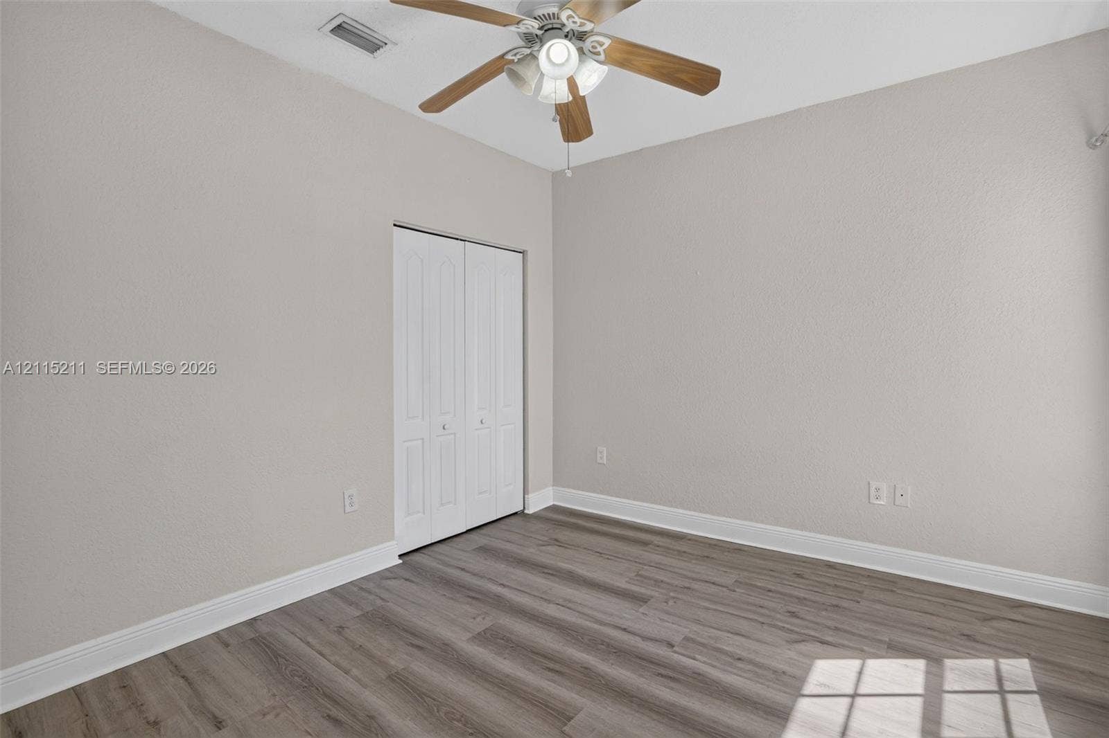 Neutral-toned interior room featuring wood-finish flooring, a multi-blade ceiling fan with integrated lighting, and a bi-fold closet door