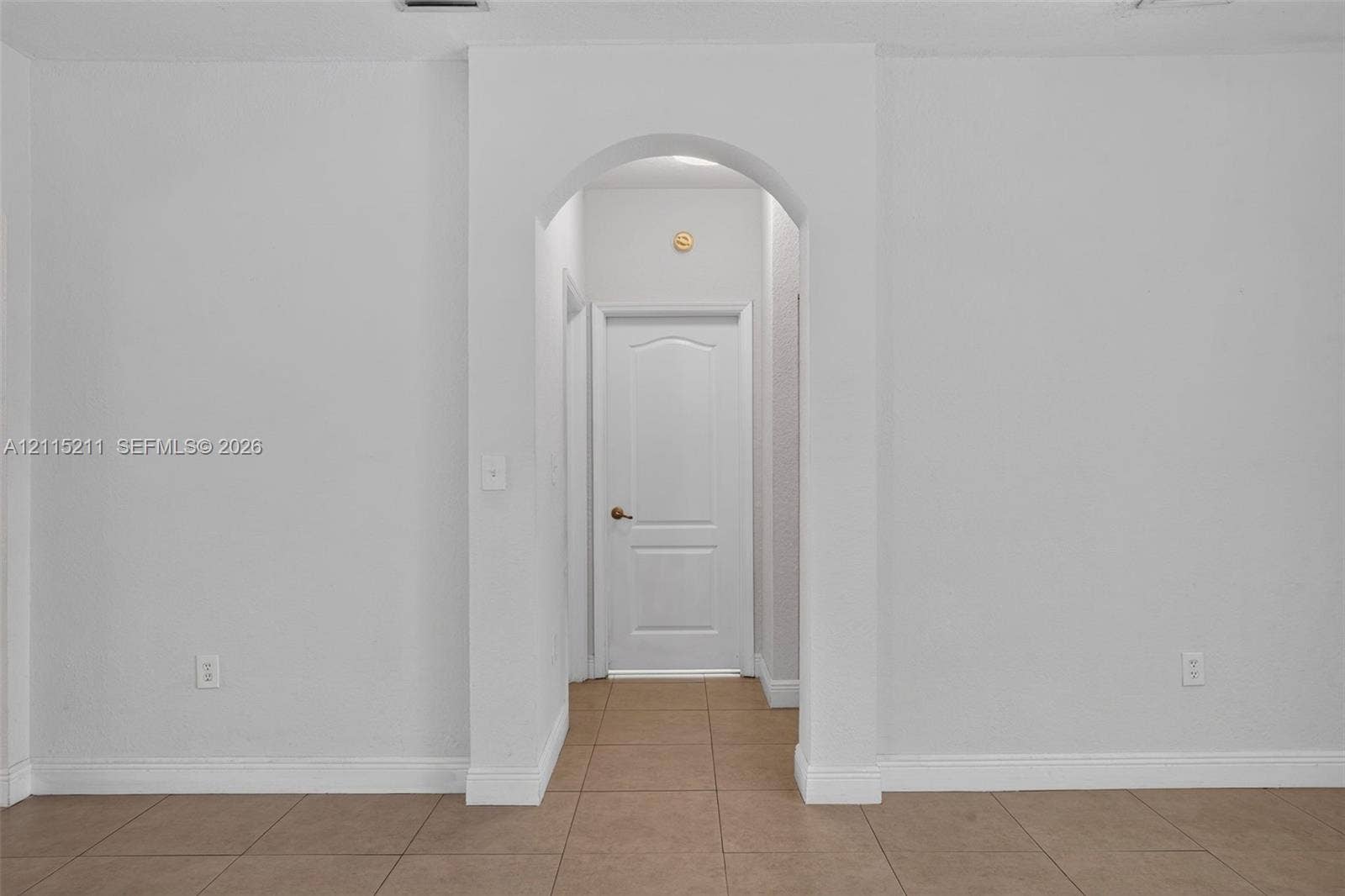 Arched doorway featuring a six-panel interior door and neutral tile flooring