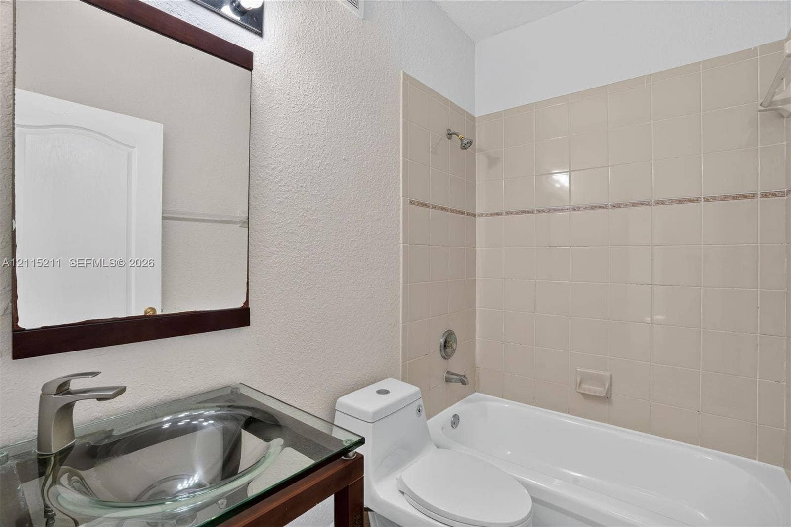 Glass vessel sink with a brushed-nickel faucet, dark-finish vanity, framed wall mirror, and tub-shower combination with ceramic tile surround