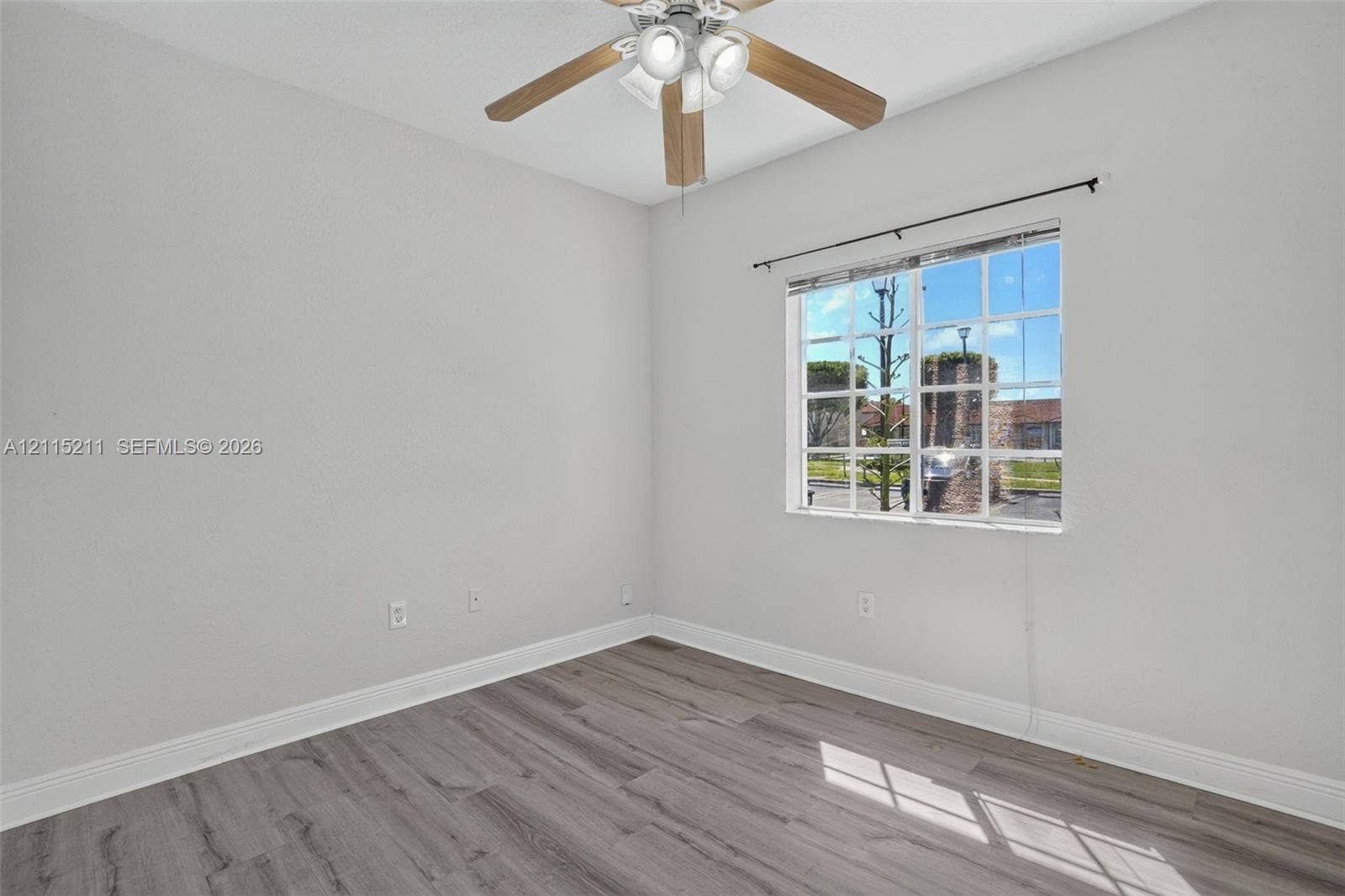 Room featuring wood-finish flooring, a multi-pane window with a curtain rod, and a ceiling fan with integrated lighting