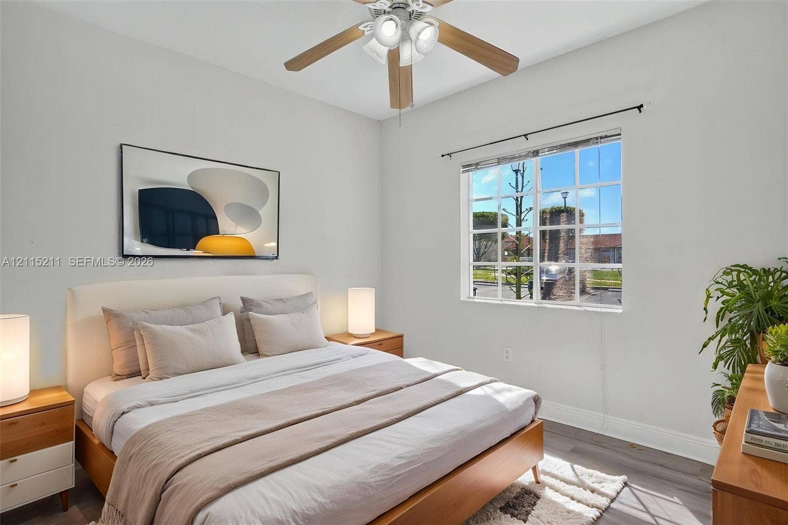 Neutral-toned interior room featuring wood-finish flooring, a multi-lite window, and a ceiling fan with integrated lighting