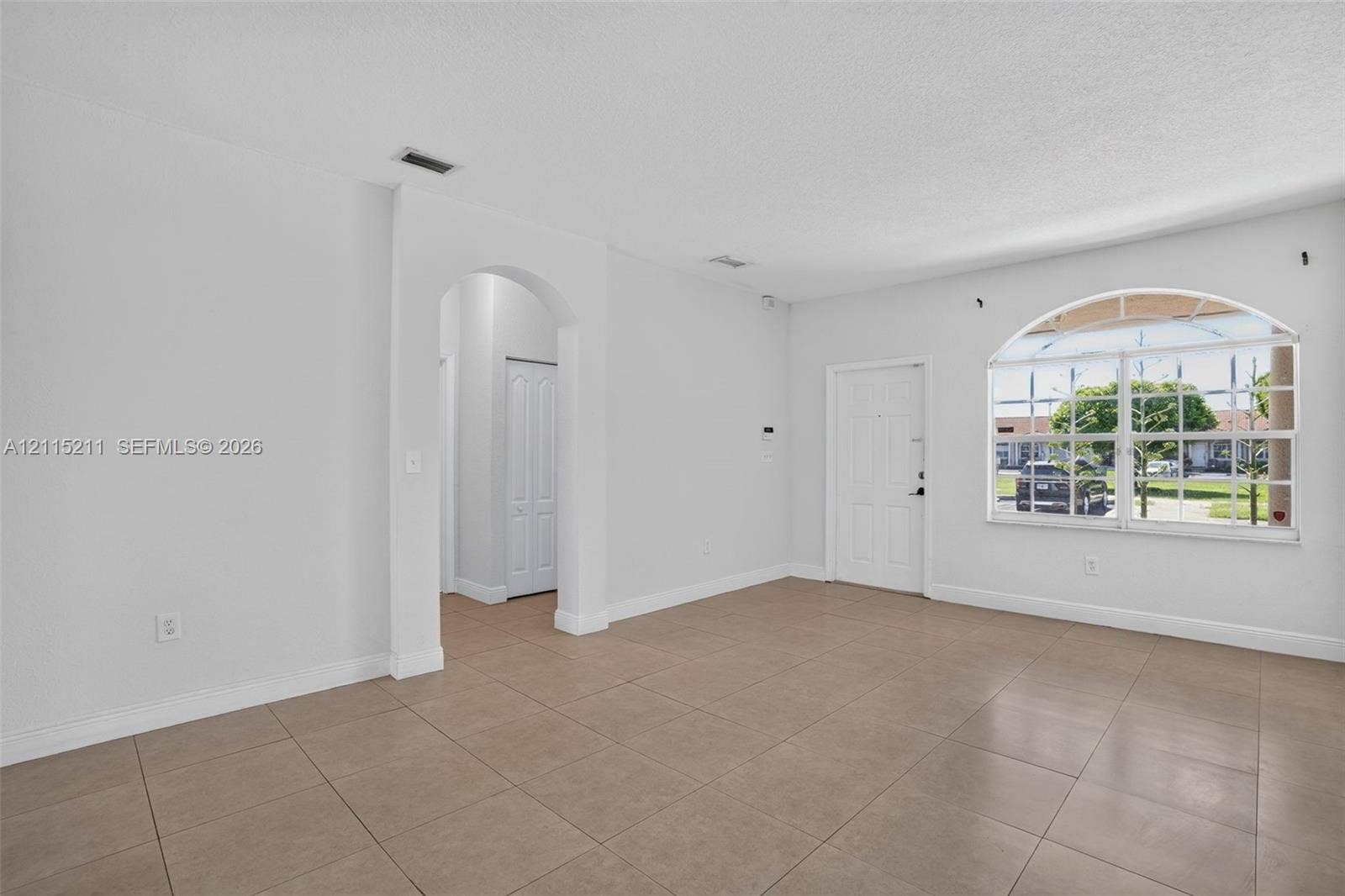 Neutral-toned ceramic tile flooring, arched entryway, and large windows featuring an arched top pane