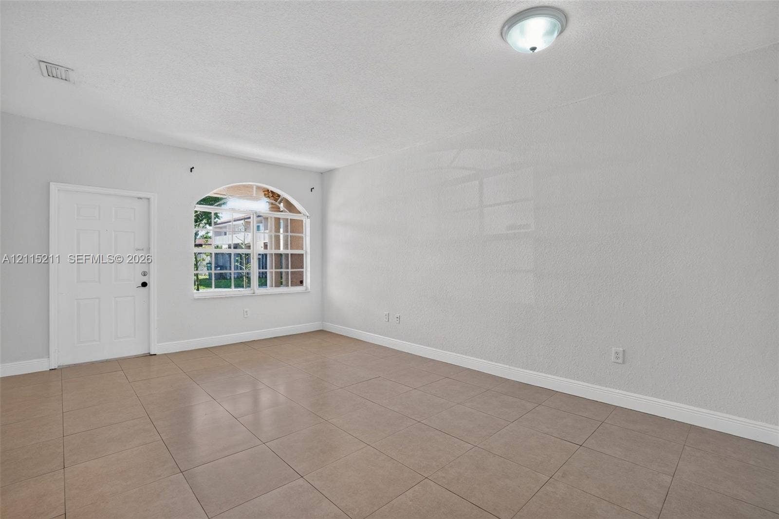 Room featuring large-format ceramic tile flooring, an arched window with multi-pane grid detailing, and a multi-panel interior door