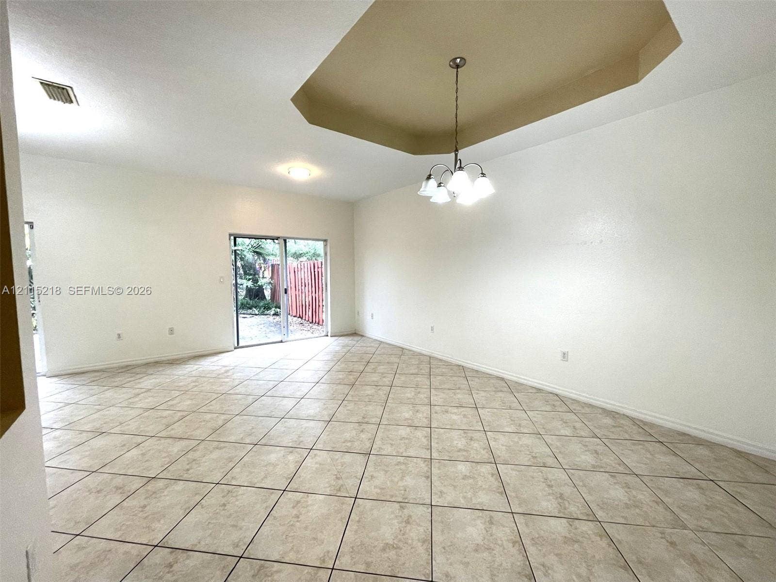 12738 SW 49th Court, #12738, Miramar, Miramar, FL 33027 Spacious interior featuring ceramic tile flooring, a recessed tray ceiling, a multi-light chandelier, and sliding glass doors leading to the exterior
