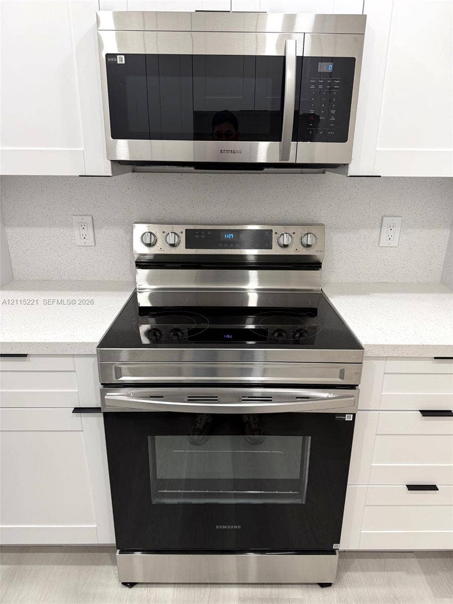 301 Bonaventure Boulevard, #15, Weston, FL 33326 Stainless steel electric range with smooth-top cooktop and matching over-the-range microwave, set between white shaker-style cabinetry, complemented by solid-surface countertops